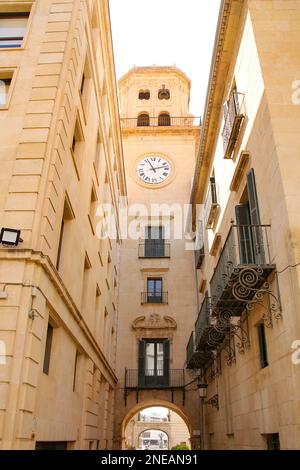 Blick hinter das Rathaus von Alicante. Uhrenturm über und schmale Gasse unter Ihnen, die zum Stadtplatz oder plaza in Alicante, Spanien führt. Stockfoto
