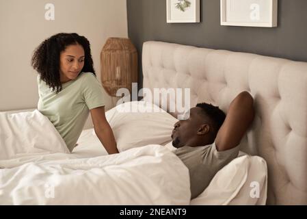 Lächelndes, junges, multirassisches Paar, das morgens im Bett spricht Stockfoto