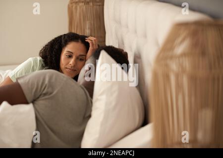 Lächelndes, junges, multiethnisches Paar, das im Bett miteinander redet Stockfoto