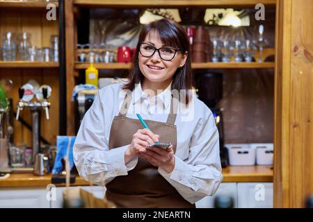 Frau, die im Restaurant arbeitet, mit Notizblock in die Kamera schaut Stockfoto