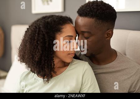 Liebevolles junges, multirassisches Paar, das in seinem Schlafzimmer sitzt Stockfoto