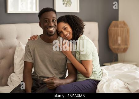 Ein junges, multiethnisches Paar, das auf dem Bett sitzt und lächelt Stockfoto