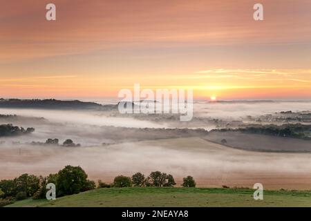 Ein nebiger Sonnenaufgang über Warminster in Wiltshire, fotografiert von Cley Hill. Stockfoto