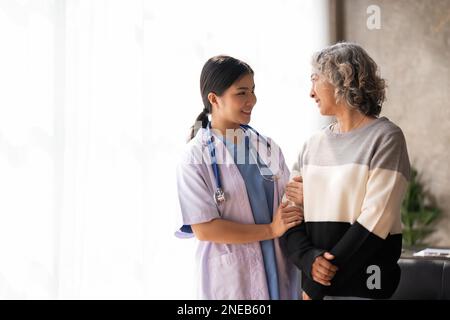 Junge Pflegekraft hilft Seniorin beim Gehen. Krankenschwester, die ihre alte Patientin im Pflegeheim betreut. Seniorin mit Gehstock, dem man hilft Stockfoto