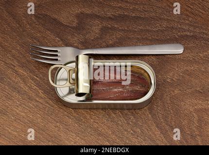 Offene Blechdose mit Sardellenfilet in Öl und Silbergabel auf Holzhintergrund. Draufsicht Stockfoto