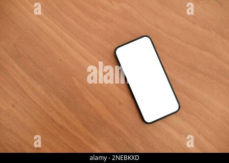 Zugeschnittene Draufsicht eines Smartphone-Modells auf dem Holztisch. Mobiltelefon mit leerem Bildschirm zur Montage des Grafikdisplays Stockfoto