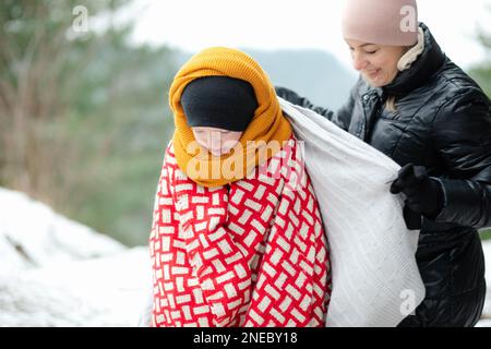 Porträt einer glücklichen Familie, die im Winter im Parkwald spaziert. Mutter mittleren Alters, die einen Teenager mit Decken deckt. Stockfoto