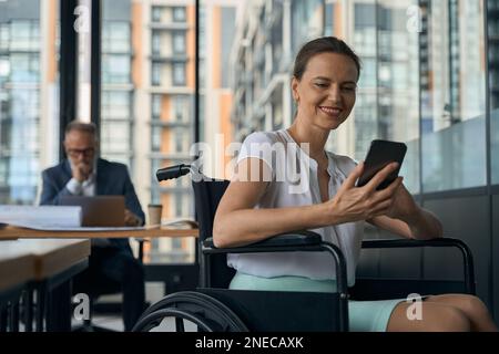 Ein Mitarbeiter im Rollstuhl chattet am Telefon Stockfoto