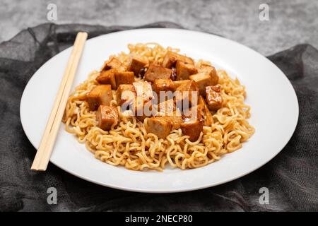 Gebratene Nudeln mit Tofu auf weißem Gericht und Stäbchen Stockfoto
