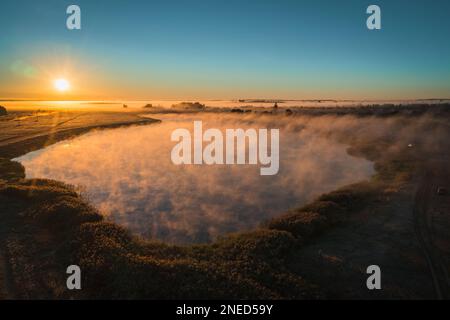 Malerische Seenlandschaft mit Nebel und wunderschöner Sonne am Horizont des blauen Himmels Stockfoto