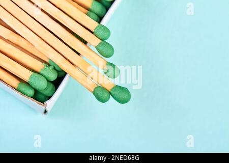 Viele Streichhölzer mit grünen Köpfen in einer Streichholzschachtel auf blauem Hintergrund mit Kopierraum Stockfoto