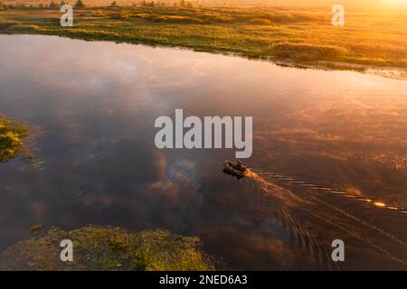 Der Fischer segelt in der Morgendämmerung mit dem Fischerboot flussabwärts in der malerischen Natur in den hellen Sonnenstrahlen der Morgensonne Stockfoto