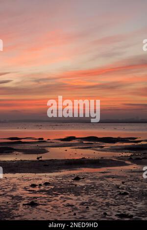 Farbenfroher Sonnenuntergang über den Schlammgebieten und dem Wasser im Hafen von Pagham, die Flut schwindet, Wildvögel- und Wattenhabitat, Sussex, Großbritannien, Februar Stockfoto