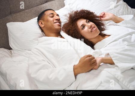 Wunderschönes, multiethnisches Paar liegt auf dem Bett im Hotelzimmer Stockfoto