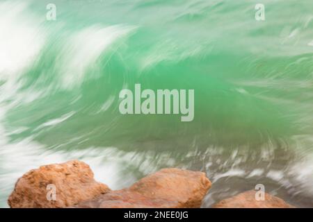 Türkisfarbenes Wasser mit Wellen und Felsen im Vordergrund. Verschwommenes Bild. ICM-Bewegung Stockfoto