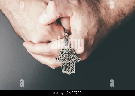 Nahaufnahme von gefalteten Händen, die Hamsa-Amulett hielten, auch bekannt als Hand von Fatima, zum Schutz vor bösem Auge, Unglück, Krankheit und Unglück Stockfoto