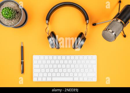 Podcasting und Podcast Aufnahmekonzept, Draufsicht von Mikrofon, Kopfhörer und Computer-Tastatur auf orangefarbenem Schreibtisch Stockfoto