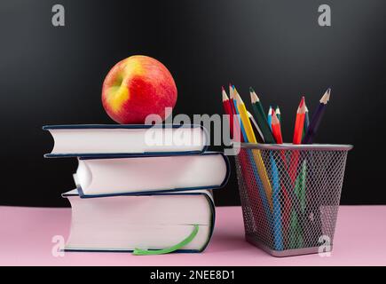 Bildungskonzept, frischer Apfel auf Bücherstapel neben Bleistiftbecher mit Buntstiften Stockfoto