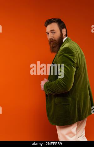 Eleganter Mann in grüner Samtjacke, der auf rotem Hintergrund auf die Kamera schaut, Stockbild Stockfoto