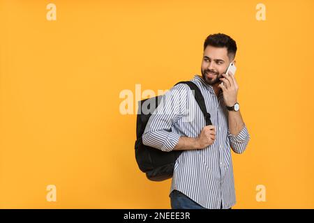 Junger Mann mit stilvollem Rucksack, der vor gelbem Hintergrund telefoniert. Platz für Text Stockfoto