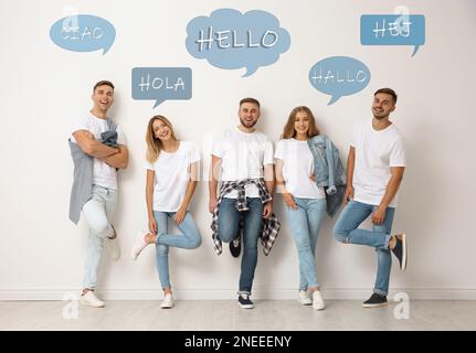 Fröhliche Leute, die neben einer hellen Wand posieren und Sprechblasen mit dem Wort „Hallo“ in verschiedenen Sprachen illustrieren Stockfoto