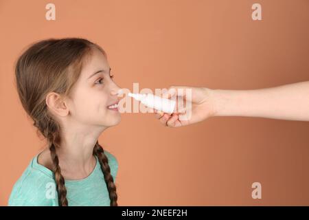 Mutter hilft ihrer Tochter, Nasenspray auf Korallenhintergrund zu verwenden Stockfoto