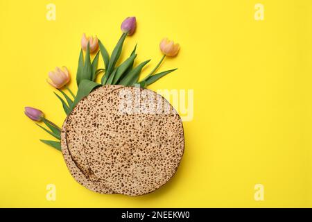 Leckere Matzen und frische Blumen auf gelbem Hintergrund, flach liegend mit Platz für Text. Pessach-Feier Stockfoto