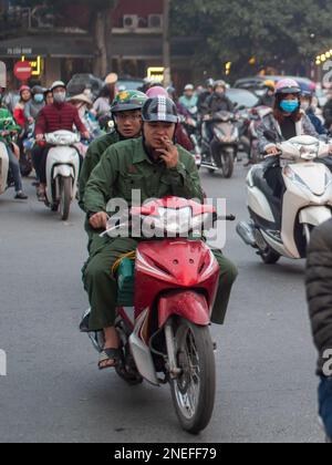 Soldaten fahren mit einem Moped durch den hektischen Verkehr in Hanoi. Stockfoto