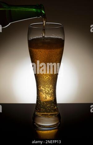 Eine Flasche Lagerbier, die in ein Glas mit Hintergrundbeleuchtung gegossen wird. Stockfoto