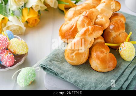 Osterfrühstück Holliday Konzept. Osterhasenbrötchen mit Zimt aus Hefeteig mit Orangenglasur, osterdekorationen, bunte Eier drauf Stockfoto