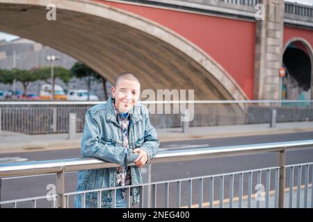 Junge Frau mit kurzen Haaren, die sich auf das Geländer einer Brücke im Freien lehnt. Konzept: Lifestyle, Empowerment, Feminismus Stockfoto