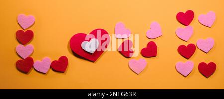 Das Konzept des Valentinstages. Die Inschrift Liebe ist auf einem gelben Hintergrund mit kleinen rosa und roten Herzen angelegt. Draufsicht. Stockfoto