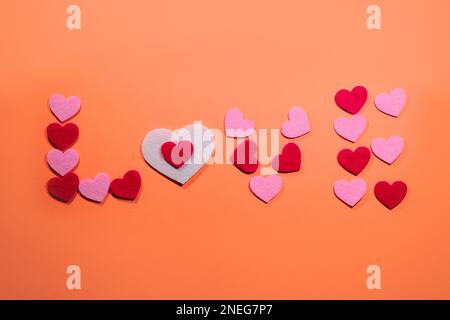 Das Konzept des Valentinstages. Die Inschrift Love ist auf einem zarten rosa Hintergrund mit kleinen rosa und roten Herzen angelegt. Blick von oben. Stockfoto