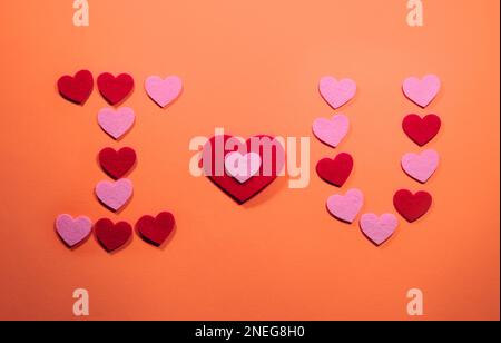 Das Konzept des Valentinstages. Die Inschrift I love you ist auf einem orangefarbenen Hintergrund mit kleinen rosa und roten Herzen angelegt. Blick von oben. Stockfoto