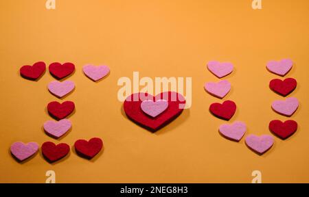 Das Konzept des Valentinstages. Die Inschrift I love you ist auf einem gelben Hintergrund mit kleinen rosa und roten Herzen angelegt. Blick von oben. Stockfoto