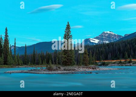 Athabasca River bei Nacht mit Sternenpfaden und roter Autoleuchte entlang der Autobahn mit Mount Edith Cavell im Hintergrund, Jasper National Park, Kanada. Stockfoto