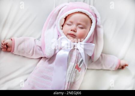 Ein Neugeborenes in einem Schlafanzug mit den Ohren eines Osterhasen ruht während eines Nickerchens mit seitlich gestreuten Armen Stockfoto