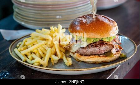 Ein frisch gegrillter Rindfleischburger mit Guacamole, serviert neben Pommes frites Stockfoto