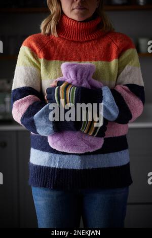 Frau In Handschuhen Umarmt Heiße Wasserflasche Versucht, Warm Zu Halten Während Der Lebenshaltungskosten Energiekrise Stockfoto