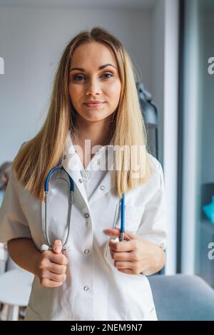 Vertikales Porträt einer jungen blonden Krankenschwester mit einem Stethoskop um den Hals Stockfoto