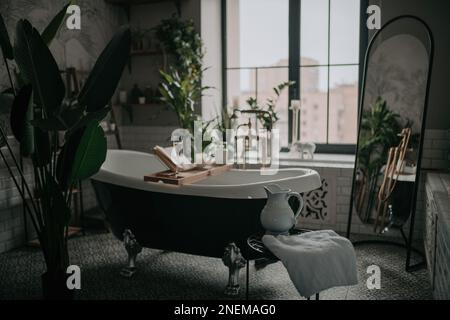 Badezimmer in einheimischen Farbtönen in organischen Formen mit großer, ovaler Badewanne in neutralen Erdtönen. Grüne Palmen Kerzen Schaumbad Pacht und Fässer Stockfoto