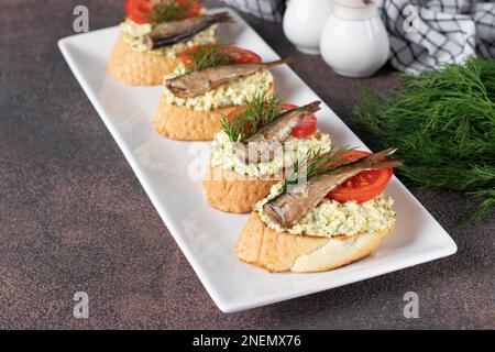 Hausgemachte Sandwiches mit Sprotten, Ei, Käse und Tomaten auf weißem Teller Stockfoto