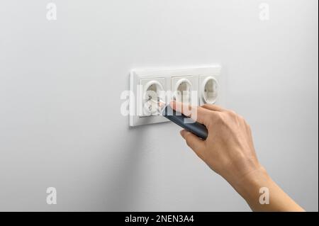 Hand hält einen berührungslosen Netzwerktester zum Messen elektrischer Daten, der zum Prüfen elektrischer Stromkreise verwendet wird. Elektrische Reparatur zu Hause. Stockfoto