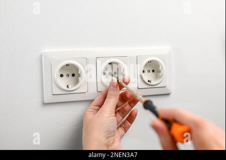 Eine Frau repariert eine Steckdose mit einem Schraubenzieher. Installation einer neuen Steckdose in der Wand Stockfoto