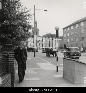 London, England. Ca. 1960. Blick auf die Harleyford Street in Kennington, Lambeth, Süd-London, mit Blick auf die U-Bahnstation Oval und St Mark's Church. Auf der rechten Seite ist Rothsay Court zu sehen und auf der linken Seite befinden sich Geländer, die vor Lockwood House verlaufen. Diese wurden aus recycelten ARP (Air RAID Vorkehrungen) medizinischen Bahren hergestellt, die während des Zweiten Weltkriegs in Massenproduktion produziert wurden, um die Verluste zu beheben, die während des Blitz entstanden waren. Auf einem Lampenträger befindet sich ein Werbeschild mit dem Slogan „Stop Unfälle – Honour Your Code“, einer Kampagne zur Straßenverkehrssicherheit aus dem Jahr 1960. Stockfoto