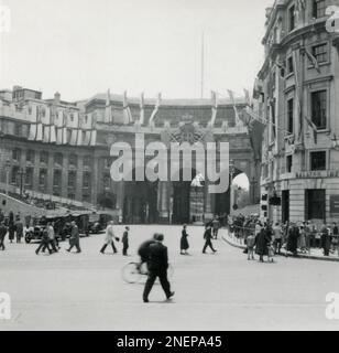 London, England. 1953. Blick auf den Admiralty Arch von der Mall, in der Nähe des Trafalgar Square. Der Bogen ist mit einer großen Fahne des Königlichen Cyphers und der Königlichen Fähnrich geschmückt, insbesondere für die Krönung von Königin Elizabeth II., die am 2. Juni 1953 stattfand. Zur Vorbereitung der Prozession wurde neben dem Bogen ein provisorischer Stand errichtet. Im Vordergrund befindet sich das Malaya House, das mit Flaggen geschmückt ist. Stockfoto