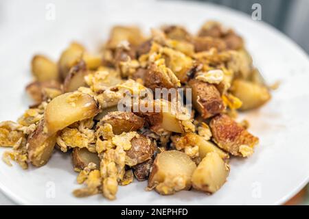 Makroaufschnitt von Frühstück oder Brunch, Kartoffelwürfel, gebratenes Hasch auf weißem Teller mit Konsistenz von gelben Rühreiern Stockfoto