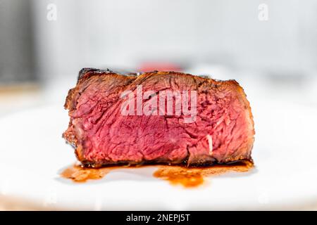 Gekochtes, seltenes, blaues rohes Streifensteak, Halbmakro-Nahaufnahme, Seitenansicht auf weißem Teller mit unscharfem Bokeh-Hintergrund und Vene Stockfoto