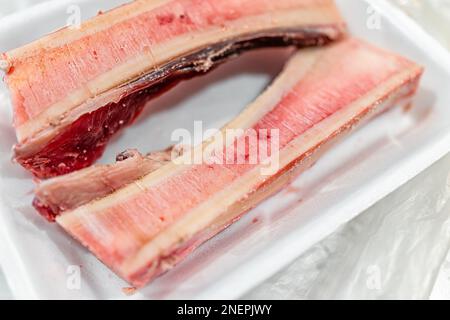 Verpackte Knochen aus rohem Rindfleisch zum Rösten von Makroaufnahmen mit einer Textur von rosa rotem Fett auf einem Plastiktablett und niemand so trendiges Essen Stockfoto
