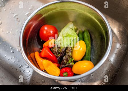 Nahaufnahme aus frisch gewaschenem rotem Blattsalat, grünen Gurken, Paprika und Tomaten für die Salatzubereitung im Waschbecken auf der Fahrt Stockfoto